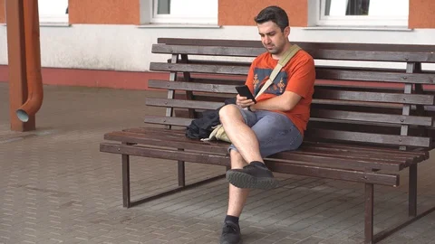 Bored man sitting on bench outside and typing in the phone Stock Footage 111860734