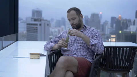 Bored man sitting on the building's roof and drinking alcoholic drink Stock Footage 87542353