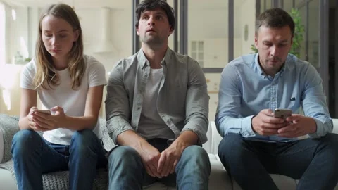 Bored man sitting on couch between gadget addicted friends with smartphones Stock-Footage 136081604