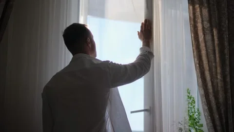 A bored man stands at a window in his house and watches what's happening Stock-Footage 311772048