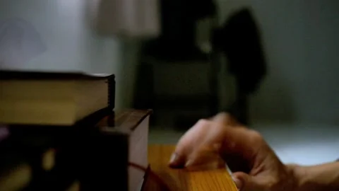 A bored man waiting is tapping his fingers on a table with a stack of books. Clo Stock Footage 289695809