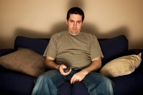 Bored, overweight man sits on the sofa Stock Photos