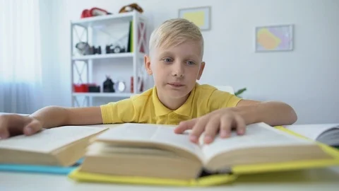 Bored schoolboy doing homework and reading books, upset kid touching head Vidéo 118987885