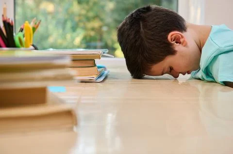 Bored schoolboy, leaning on the table with his forehead, having difficulty Stock Photos