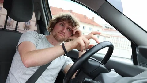 Bored young driver passes time waiting alone inside his parked car Stock Footage 343720625