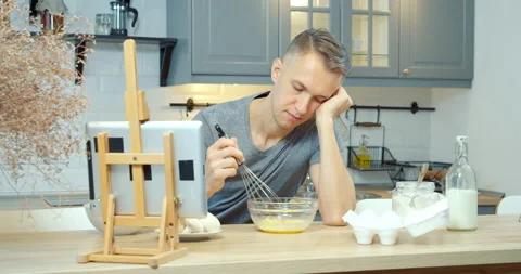 Bored young man beating eggs while preparing an omelet or dough for pancakes Stock Footage 132211734
