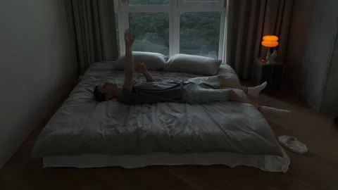 Bored young man lying on bed and tossing a small ball in the air while killing Stock Footage 312326548