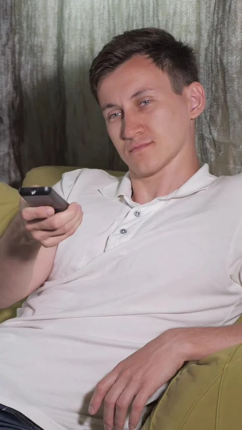 Bored young man sitting on couch changing television channels with remote Stock Footage 341440586
