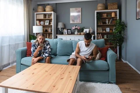 Boredom Concept. Young couple using smartphones, sitting on couch at home, .. Stock Photos