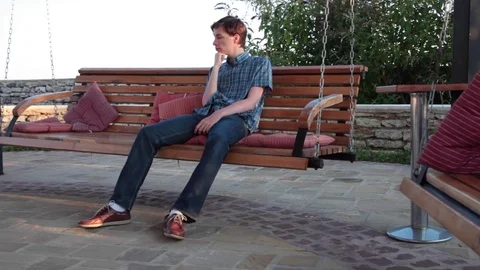 Bored/pensive young  man on a gazebo swing on a summer day Stock Footage 70573304