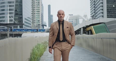 Boss in stylish brown suit walks with confident gait along busy street in Stock Footage 276524920