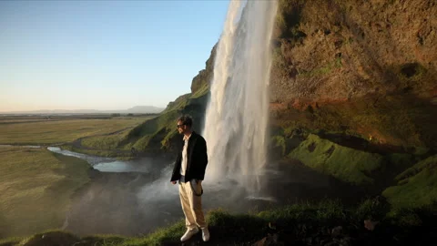 Bossy-looking man standing in front of famous Seljalandsfoss waterfall, Iceland Stock Footage 254451491