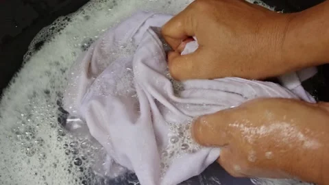 Both hands scrubbing white clothes in a basin filled with soapy foam water Stock Footage 330037441