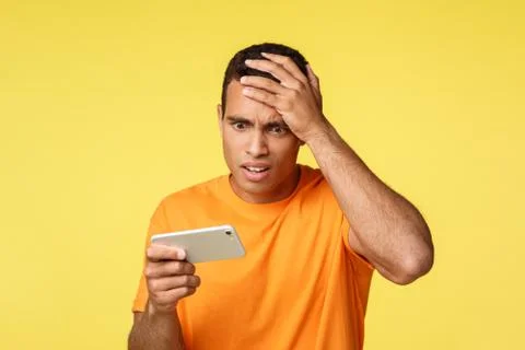 Bothered and upset shocked young handsome man, holding smartphone horizontally Stock Photos