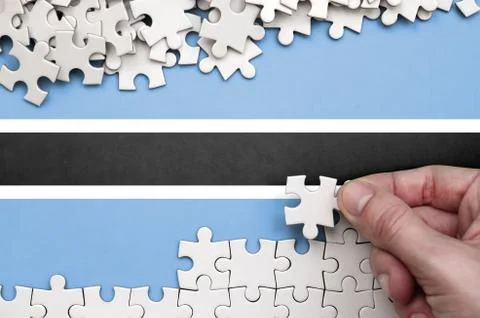 Botswana flag  is depicted on a table on which the human hand folds a puzzle  Foto stock