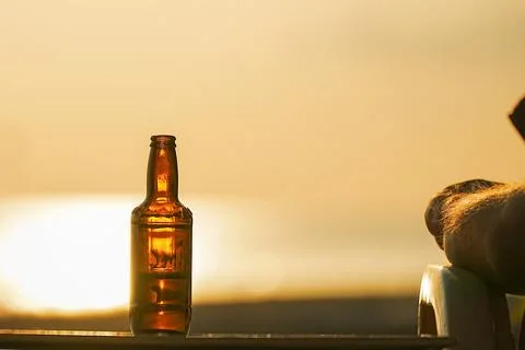 A bottle of beer on the table during sunset at sea is illuminated by the or.. Stock-Fotos