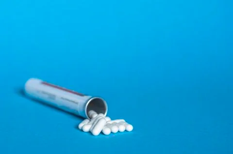 A bottle with a bunch of white capsules of tablets on a blue background. Stock Photos
