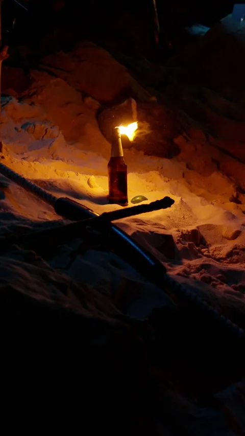 A bottle with a burning flame stands upright on illuminated sand, surrounded by Stock-Footage 310491118