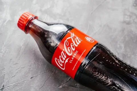 Bottle of Coca-Cola lie on gray surface with unique refreshing taste inscription Stock Photos