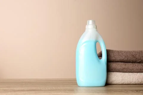 Bottle of detergent and clean towels on table against color background, space Stock Photos