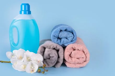 Bottle of detergent with clean towels and flowers on blue background. Plastic Stock Photos