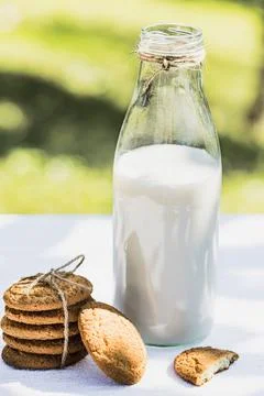 Bottle of fresh milk and stack of cookies on a white table outdoors Stock Photos