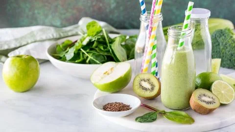 A bottle of green smoothie surrounded by ingredients used to make it. Stock Photos