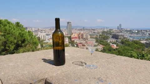 Bottle half of wine and empty glass stand on stony parapet against cityscape 스톡 동영상 151720031