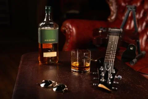 A bottle of Irish whiskey, with a glass, glasses, and a guitar on the table. Stock Photos