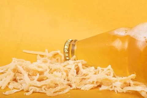 Bottle of light beer with dried squid on yellow background close-up, salty Stock Photos