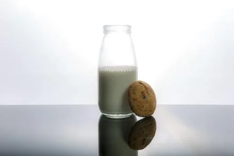 Bottle of milk and a cookie. White background, dark surface. Stock Photos