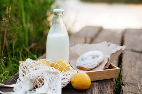 A bottle of milk and a string bag with fruit on wooden boards on the lake Foto stock