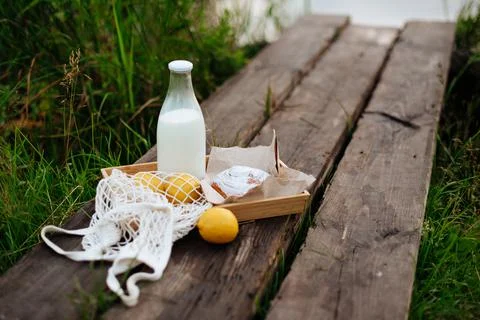A bottle of milk and a string bag with fruit on wooden boards on the lake 스톡 사진
