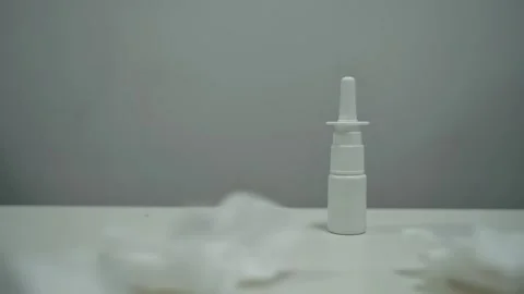 Bottle of nasal spray on a white table, then used paper napkins begin to fall on Stock Footage 270522080