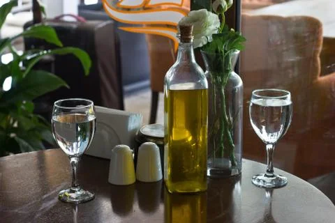 A bottle of olive oil on the table. Two glasses of water. Vase with Flowers.  Foto stock