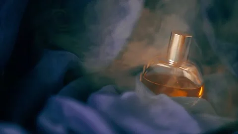 Bottle of perfume on blue fabric in cloud of smoke. Close-up slow motion video. Stock Footage 170971090