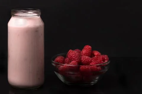 A bottle of raspberry yogurt with a transparent raspberry bowl Foto stock