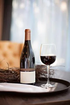 A bottle of red wine and a full glass on a tray stand on a table Stock Photos