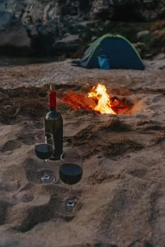 Bottle of red wine and two glasses on beach near campfire. Stock Photos