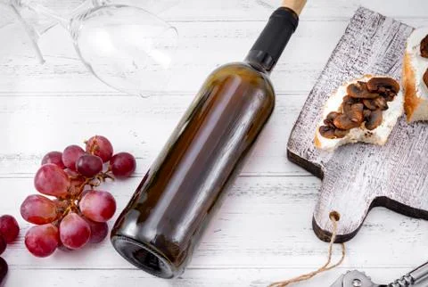 Bottle of red wine, grapes, appetizer with cheese and mushrooms, empty glasse Foto stock