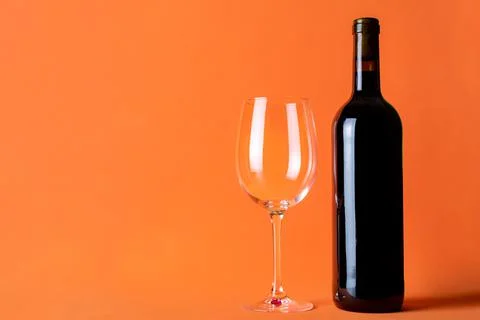 Bottle of red wine next to an empty glass on an orange background. Copy space Stock Photos