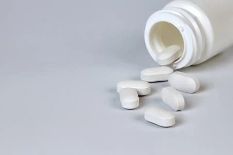 A bottle with scattered tablets on a gray background Stock Photos