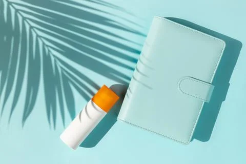 Bottle of sunscreen and notepad with palm leaf shadow on blue background Stock Photos
