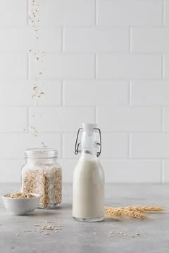 A bottle of vegetable milk in the background oat flakes are flying into the jar. 스톡 사진