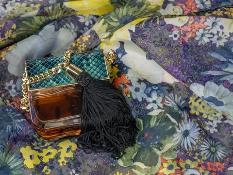A bottle of women's perfume on a background of multi-colored motley fabric. A Stock Photos