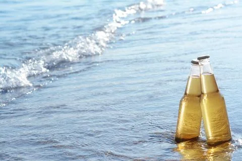 Bottles of cold beer on sandy beach near sea, space for text Fotos Stock