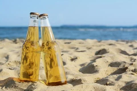 Bottles of cold beer on sandy beach near sea, space for text Foto stock