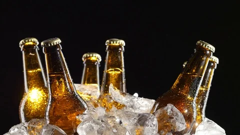Bottles with dark beer to spin in pieces of ice. Black background. Close up Stock Footage