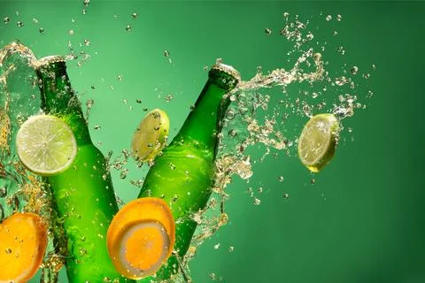 Bottles of fruit beer with splash around on green background. Stock Photos