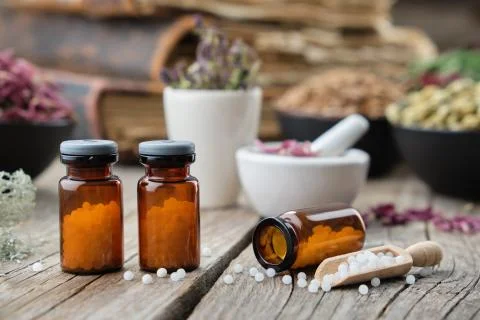 Bottles of homeopathic globules, books, mortars and bowls of healing herbs. Stock Photos